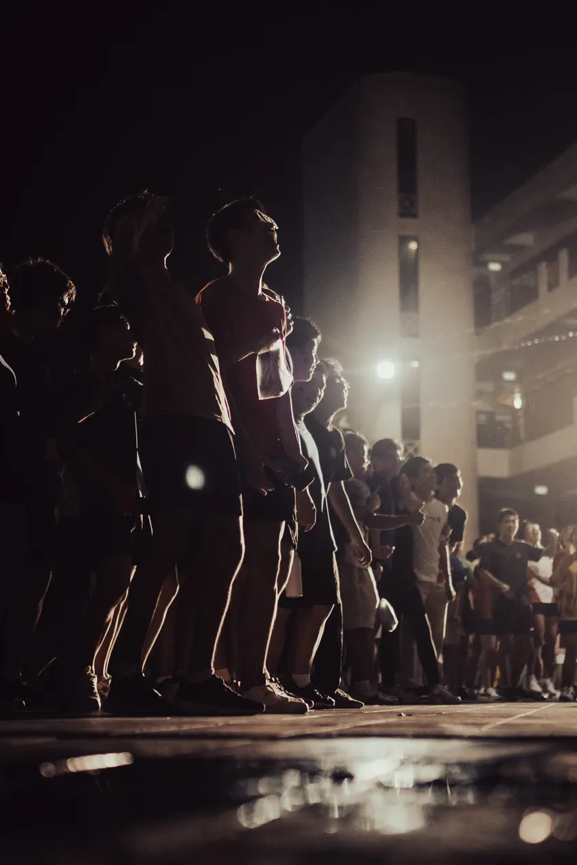 A line of students watching a night performance, rim-lit by stage lights