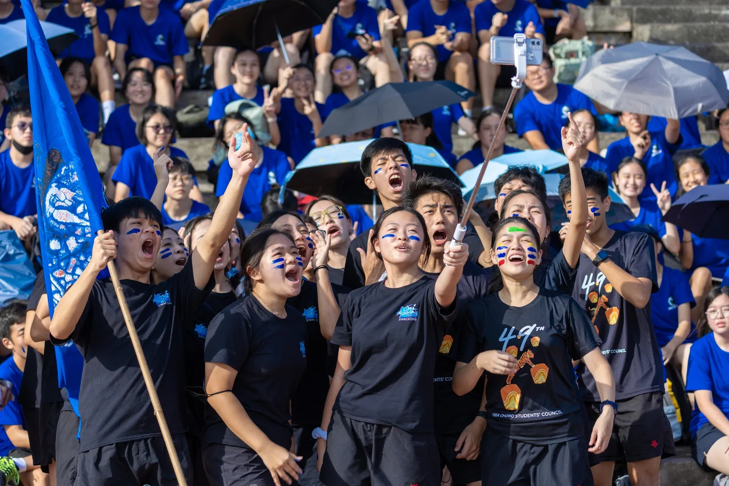 A university team in blue cheering together at an outdoor event