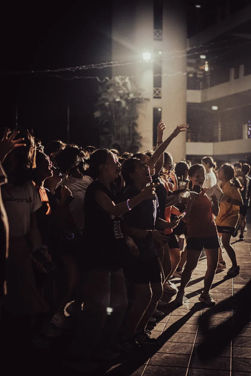 Students in a nighttime crowd reaching toward a bright stage light