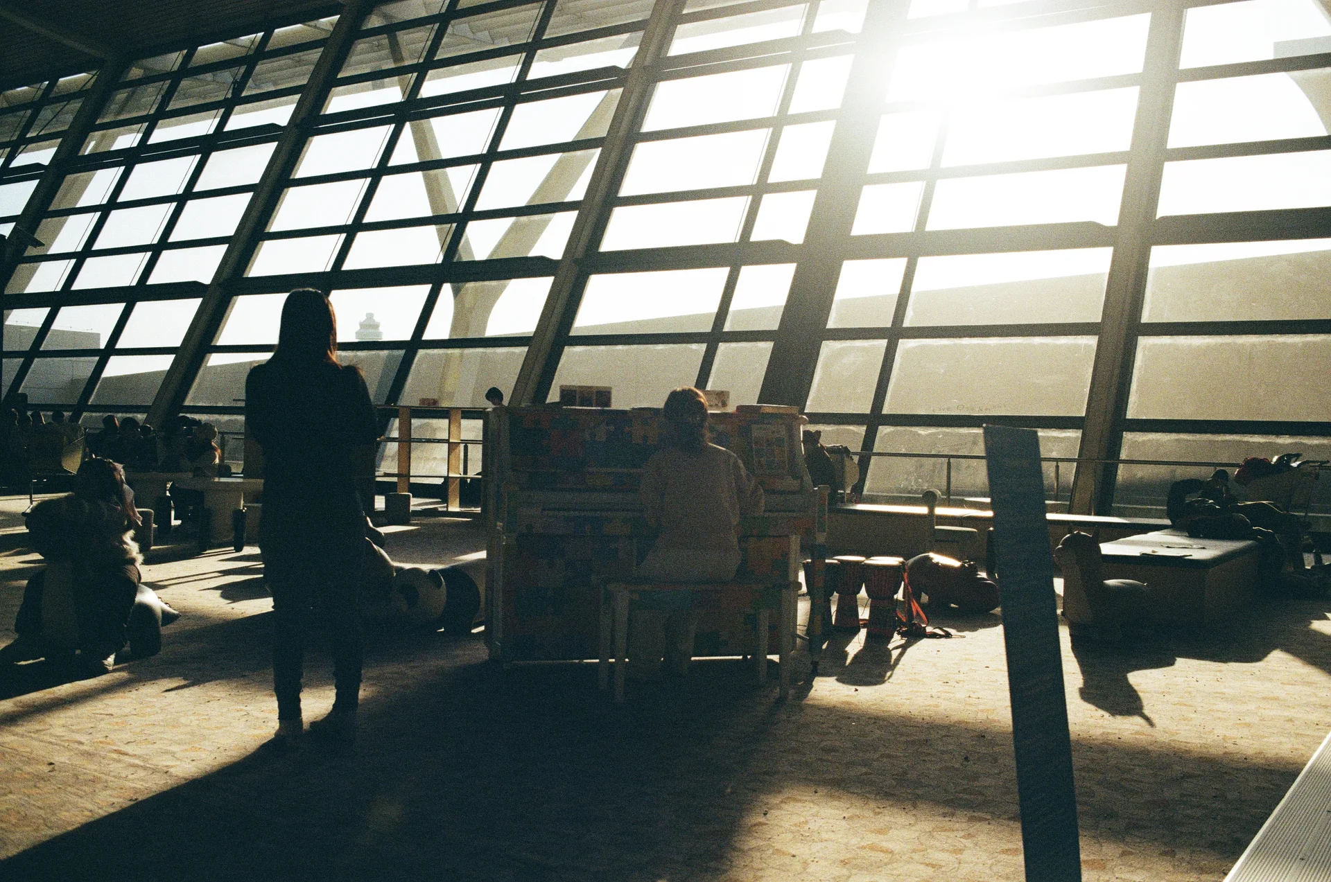 Travellers resting in a sunlit airport terminal beneath a geometric wall of windows