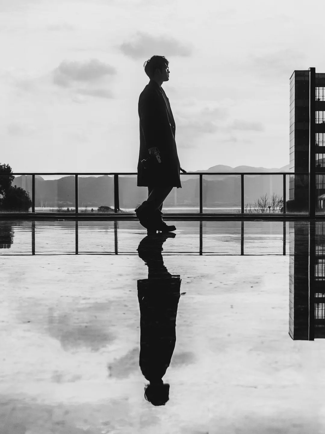 A solitary figure reflected on a wet rooftop beneath an overcast sky